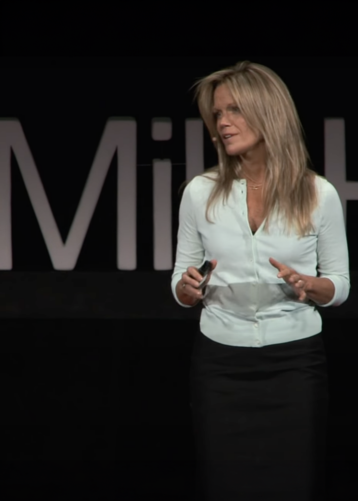 Robyn O'Brien speaking on the TEDx Mile High stage. She is wearing a mint green 3/4 sleeve shirt and black pants and gesturing with her hands.